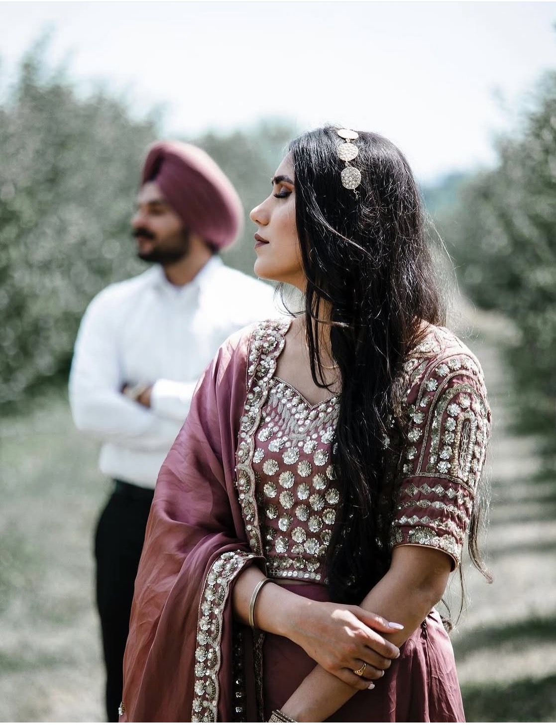 A bride in embroidered pink attire with the groom softly in the background
